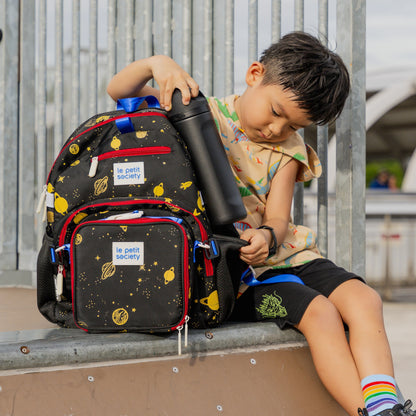 A kid with the LPS single pocket school bag in a black and yellow planet print.