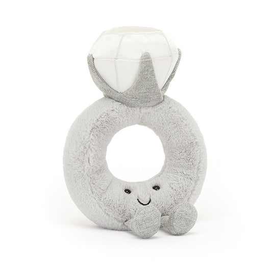 A front view of a soft, plush toy shaped like an engagement ring, with a smiling face and sparkly diamond on top. The light gray fabric gives it a cute, endearing look, making it perfect for babies or as a decorative piece.