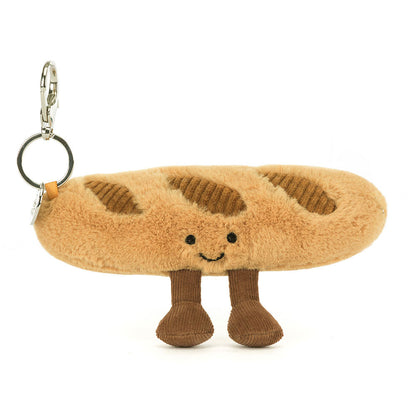 A front view of a plush baguette keychain with embroidered smile, soft brown legs, and corduroy accents, complete with a silver clip for easy attachment.