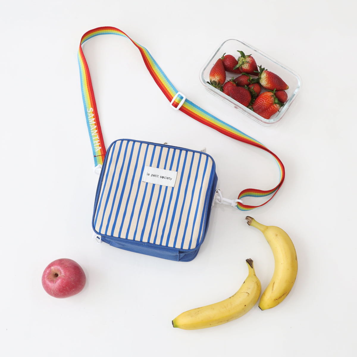 Le Petit Society's thermal lunch bag with blue stripes, a rainbow strap and snacks.