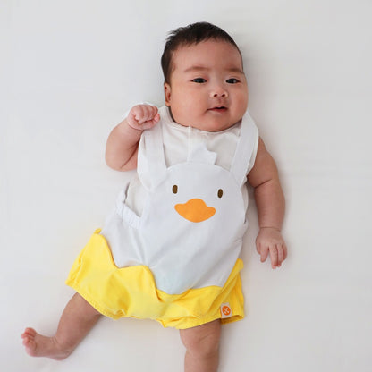 An animal-themed baby romper by Le Petit Society, featuring a duck's face at the front, complete with bright yellow bottoms and white cross back straps over a white base.