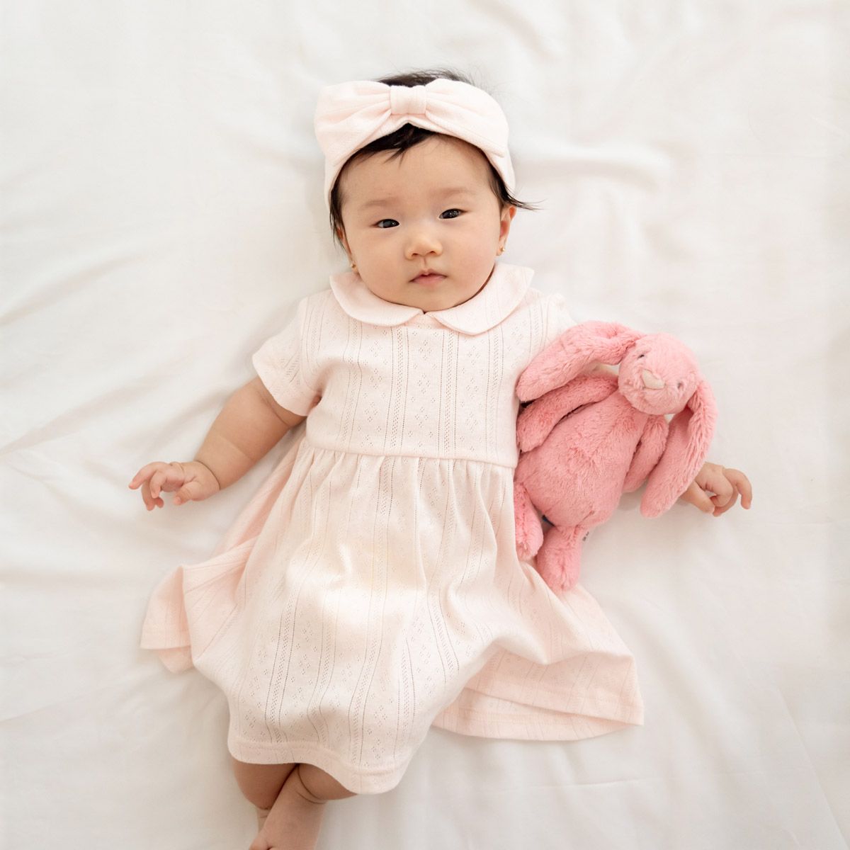 A baby girl wearing a pink dress in pointelle cotton by Le Petit Society.