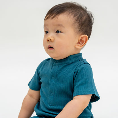 A baby boy wearing a rib knit romper in forest green from Le Petit Society.