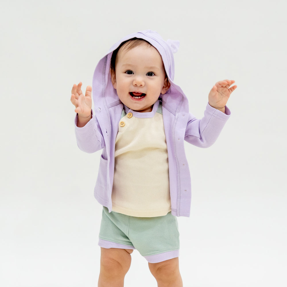 A baby boy wearing a coordinating set of a colour block tee and boxers, complete with a lilac purple bunny cardigan from Le Petit Society.