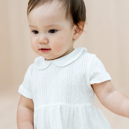 A baby girl wearing a peter pan collar dress in white pointelle cotton.