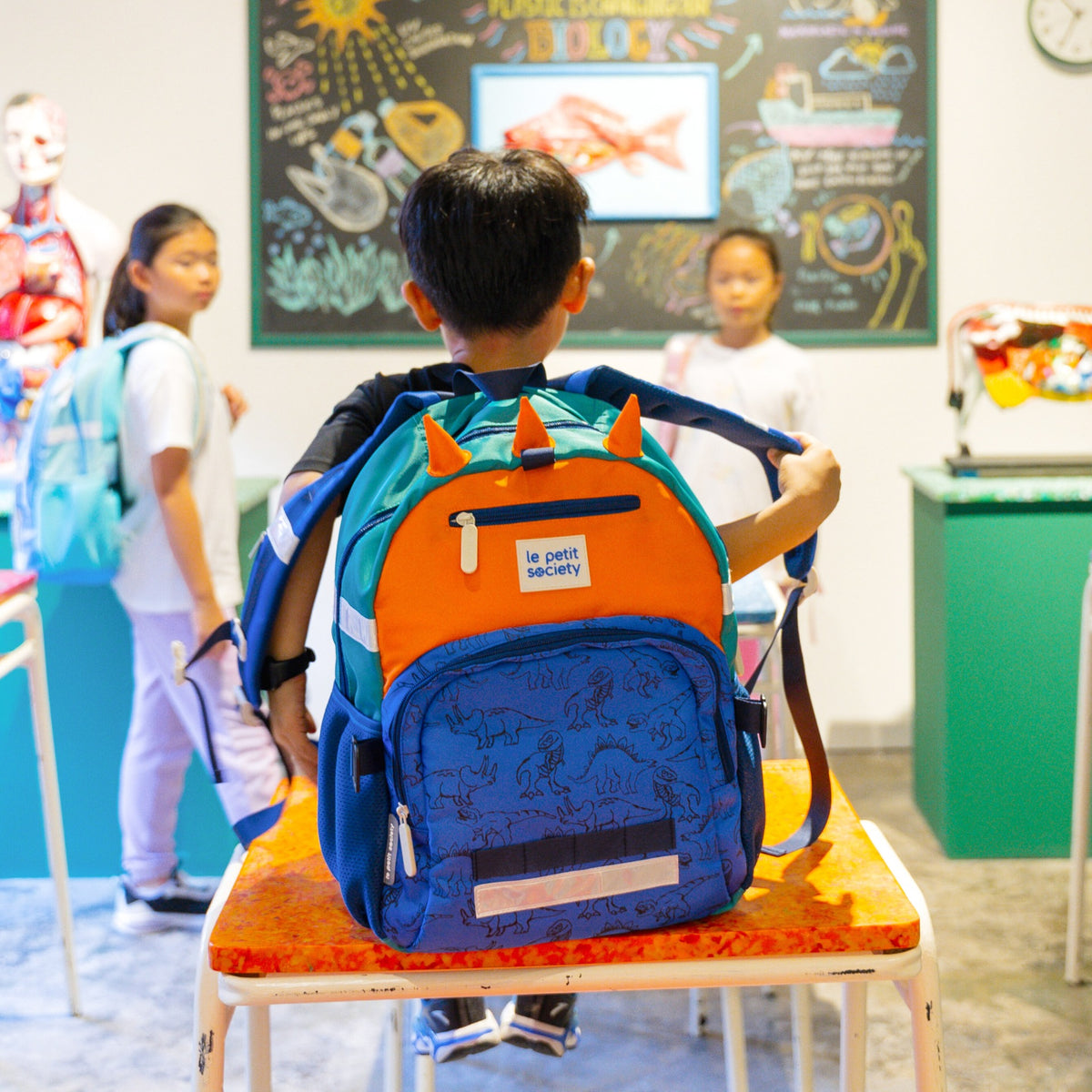 A little boy in class with the LPS kids single pocket school bag in dinosaur print.