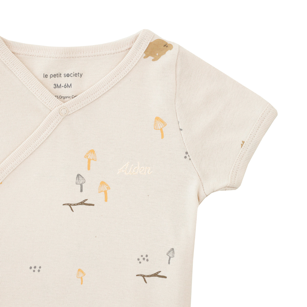 A close-up of a personalised name embroidery on a A beige-coloured baby kimono romper by Le Petit Society, featuring a woodland motif with brown rabbits.