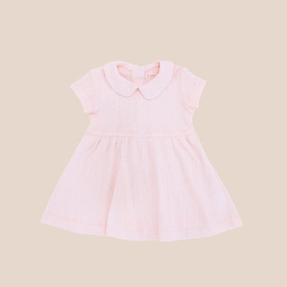 A baby girl dress from Le Petit Society. It comes with a peter pan collar and is made in a pink pointelle cotton.
