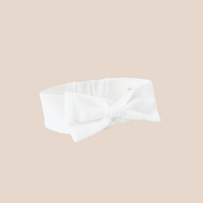 A baby headband from Le Petit Society. It is made from a white pointelle cotton fabric and comes with a large bow in the middle.