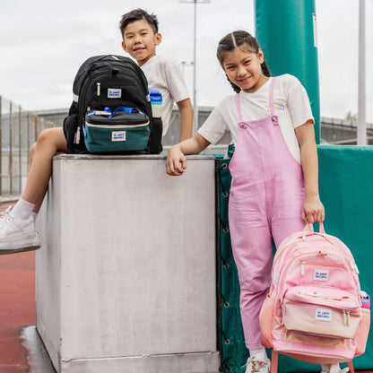 Two primary schoolers carrying school bag and lunch bag bundles from Le Petit Society.