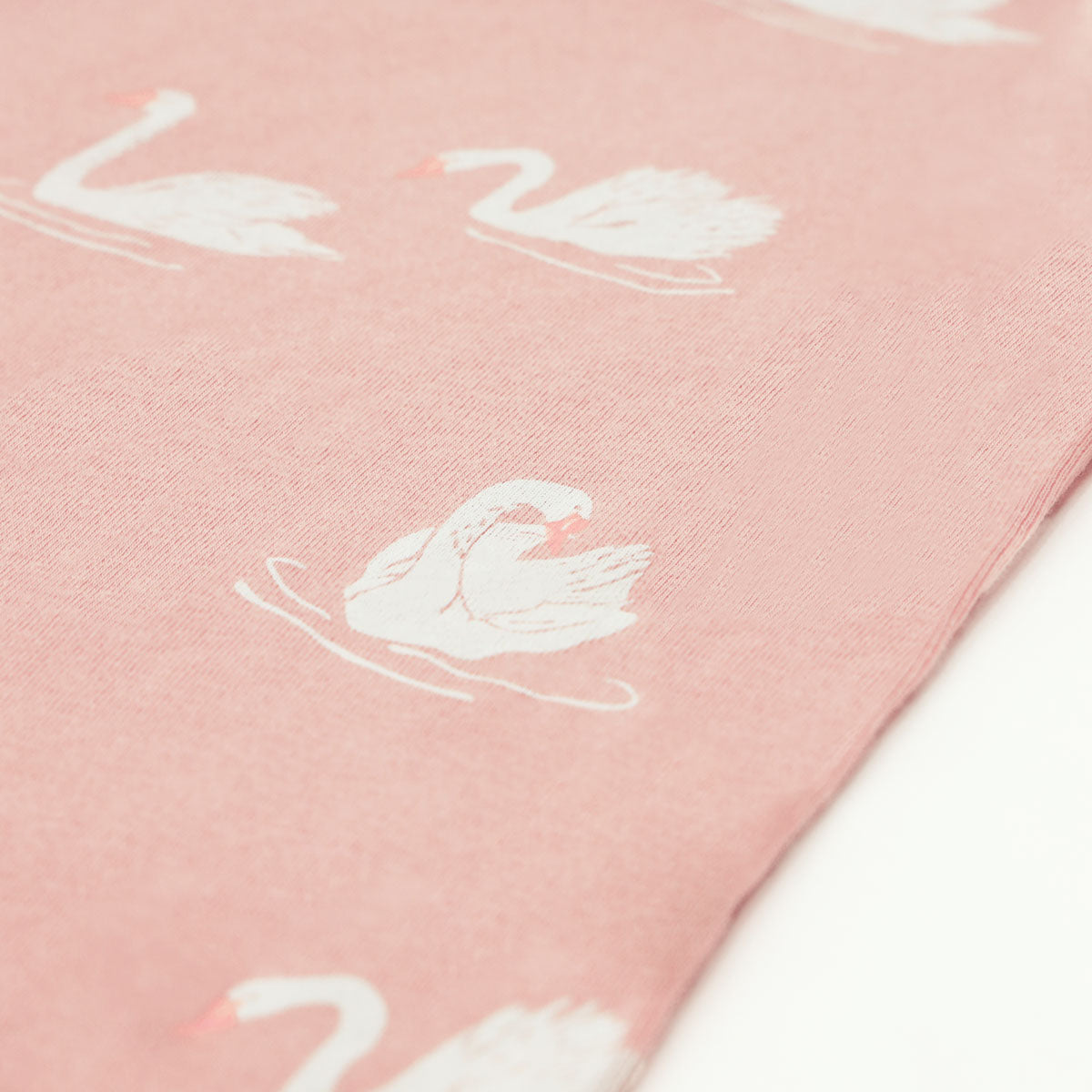 A close-up of the print of a peach-coloured baby kimono romper by Le Petit Society, featuring a print of swans.
