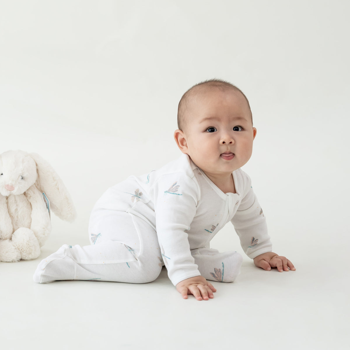 A baby wearing an organic zip sleepsuit in dragonfly print from Le Petit Society.