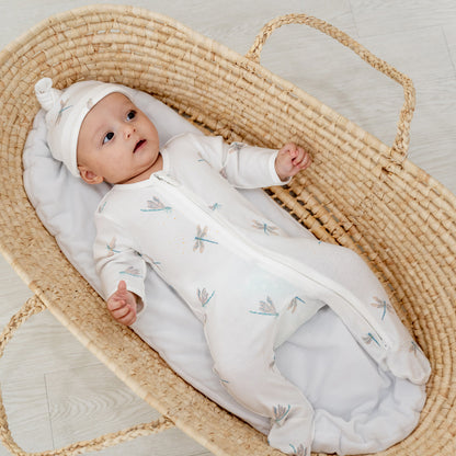 A baby wearing a matching hat and zip sleepsuit in dragonfly print by Le Petit Society.