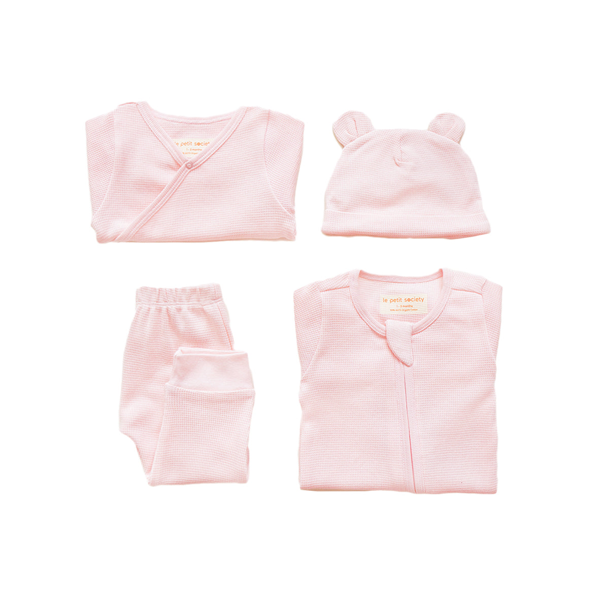 A baby organic essentials set in pink by Le Petit Society, consisting of a zip sleepsuit, kimono romper, leggings and bear hat.