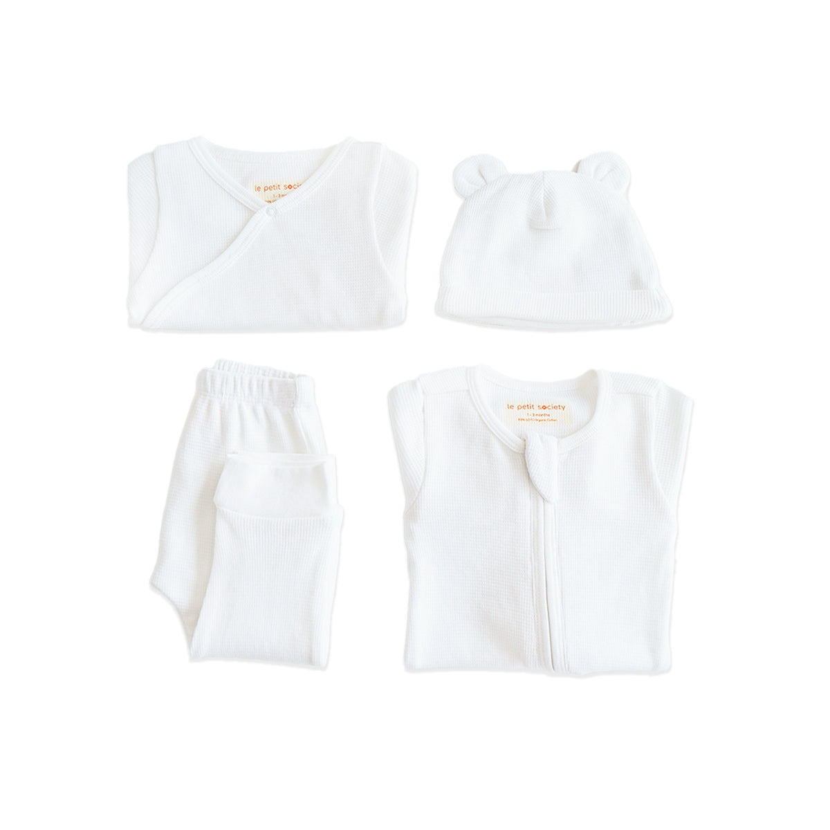 A baby organic essentials set in white by Le Petit Society, consisting of a zip sleepsuit, kimono romper, leggings and bear hat.