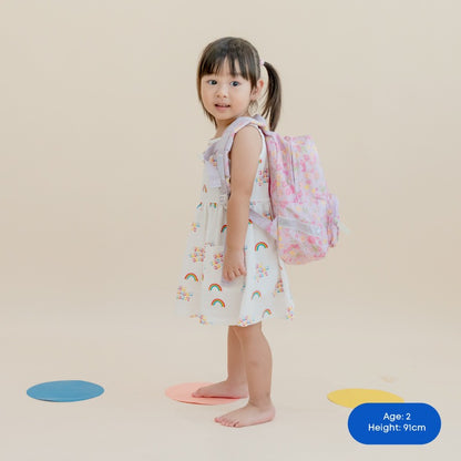 A toddler carrying a purple, floral-print preschool bag.