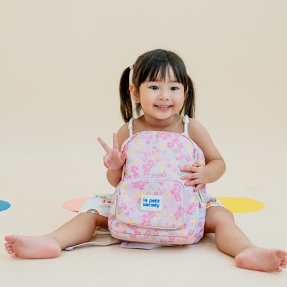 A toddler with a purple, floral-print preschool bag.