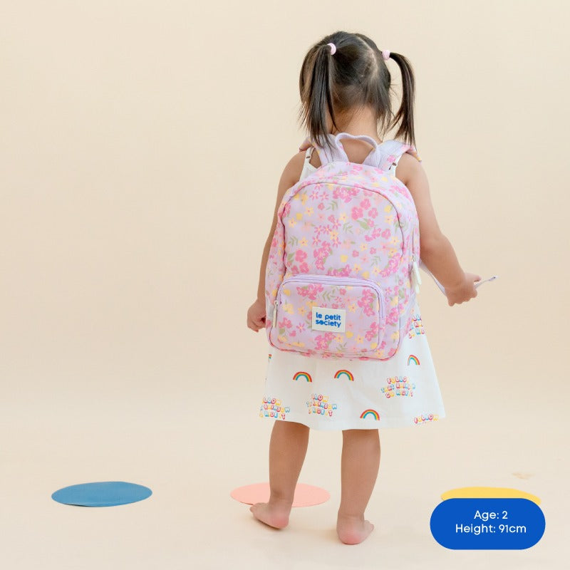 A preschool girl carrying a purple school bag with a floral print.