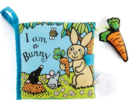 This is a soft fabric book titled "I am a Bunny" features a bunny holding a carrot in a grassy, flower-filled scene. Next to the bunny, there is a mole and a mouse, with a bee flying above