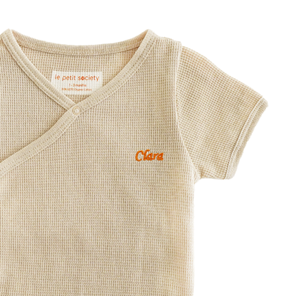 A close-up of a name embroidery personalisation on an organic, baby kimono romper in beige by Le Petit Society.