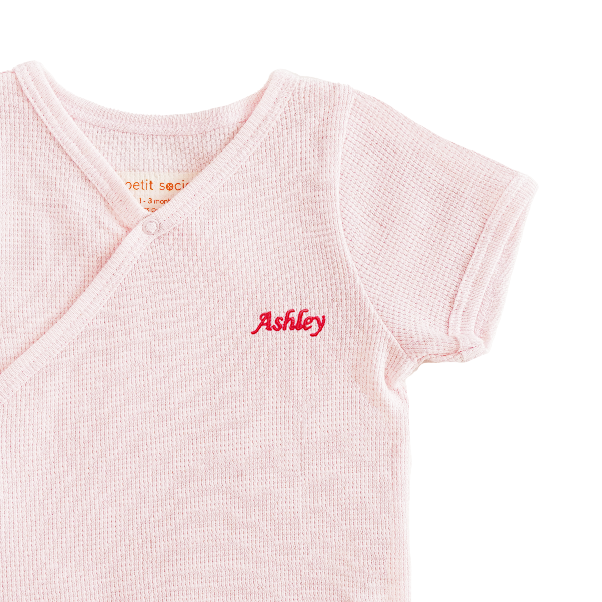 A close-up of a name embroidery personalisation on an organic, baby kimono romper in pink by Le Petit Society.
