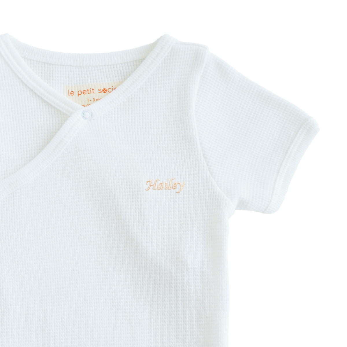 A close-up of a name embroidery personalisation on an organic baby kimono romper in white by Le Petit Society.