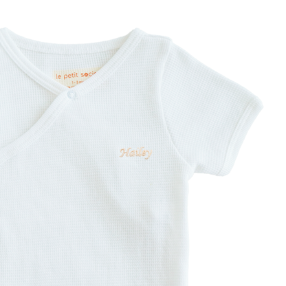 A close-up of a name embroidery personalisation on an organic baby kimono romper in white by Le Petit Society.