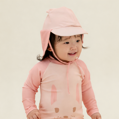 Baby wearing Le Petit Society Baby Bunny Sunhat and matching pink bunny rash guard swimsuit