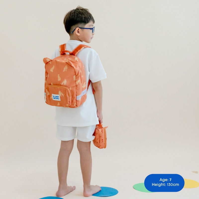 A primary school boy carrying an orange, leopard-print school bag and pencil case.
