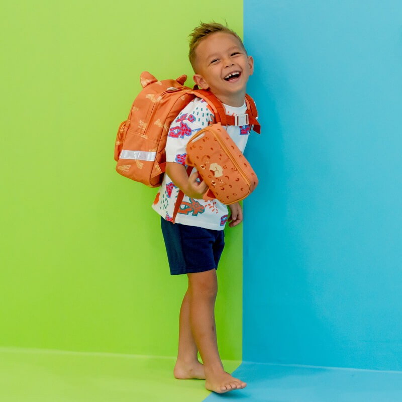 Preschool boy smiling while carrying an orange school bag and pencil case in tiger design.