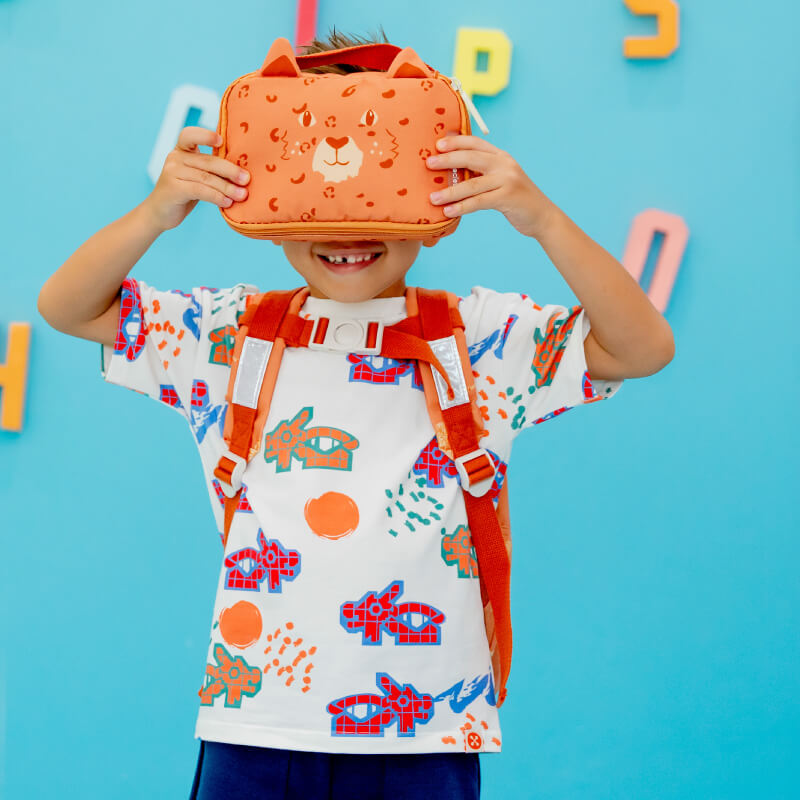 A preschooler holding up an orange pencil case with a leopard print and pair of animal ears.