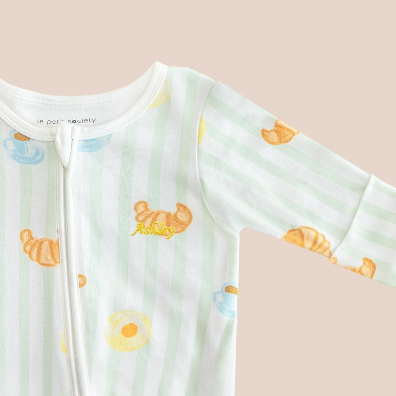 A close-up of a name embroidery personalisation on a baby bamboo sleepsuit in breakfast print by Le Petit Society.