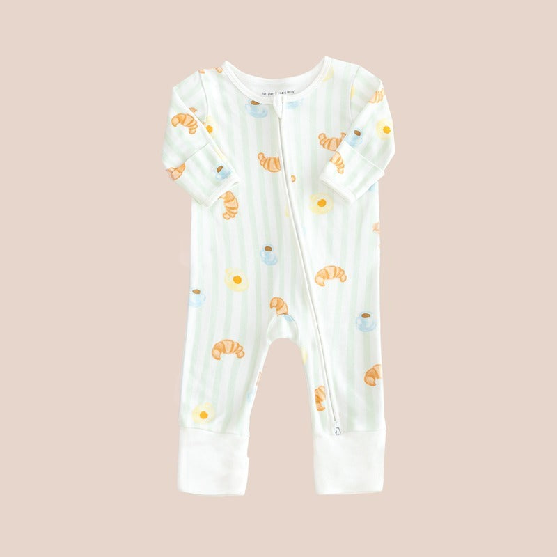A baby bamboo sleepsuit with green stripes and a print of breakfast food: croissants, coffee and sunny side-up eggs.
