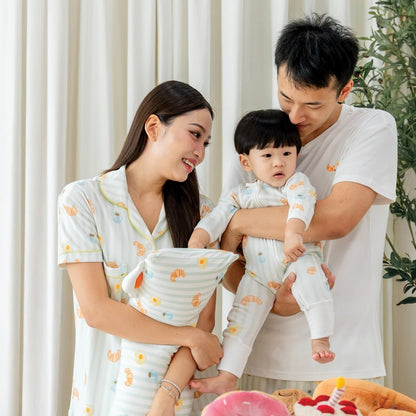 A family of three — mother, father, and baby boy — wearing coordinated breakfast print outfits from Le Petit Society, featuring illustrations of breakfast foods. 