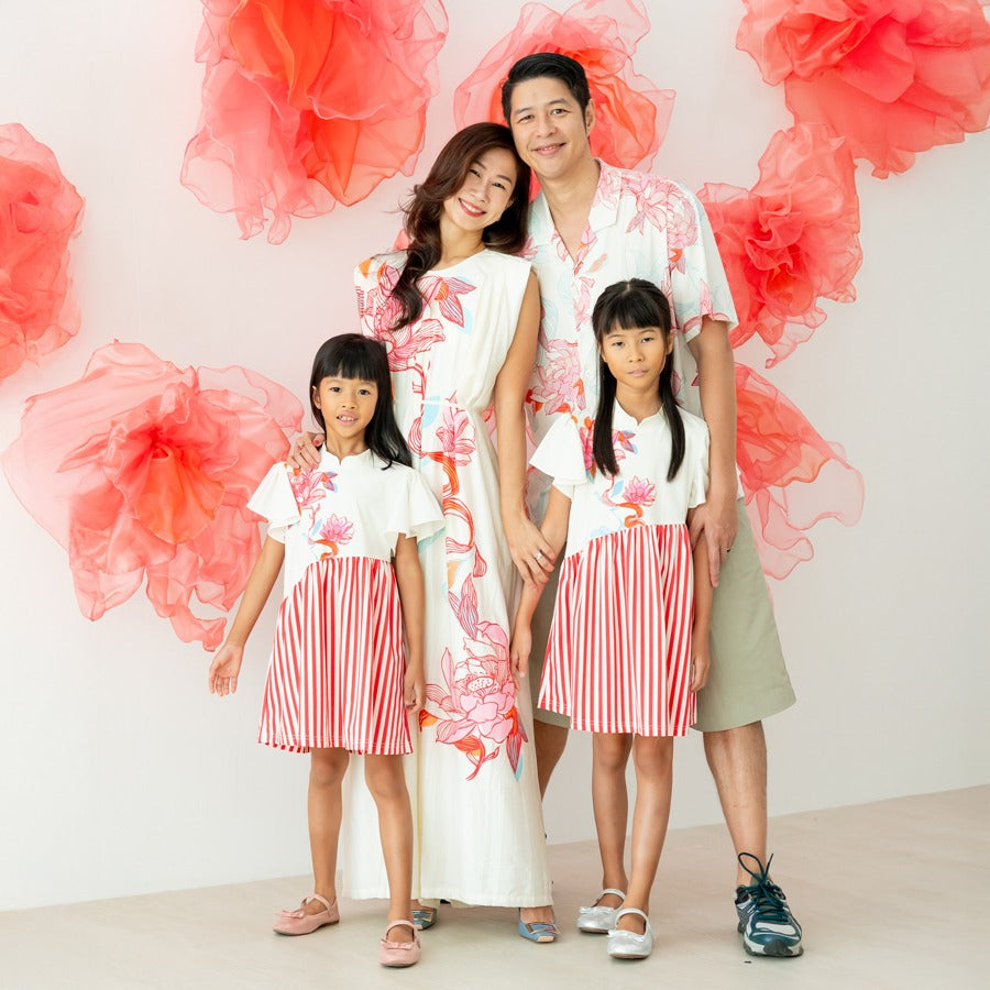 A family of four stands in coordinated outfits from the Le Petit Society x Sheila Sim CNY 2026 lotus collection. The mother wears a long cream dress with a bold floral print, while the father wears a matching cream shirt with lotus motifs and khaki shorts