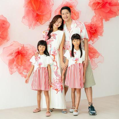 A family of four stands in coordinated outfits from the Le Petit Society x Sheila Sim CNY 2026 lotus collection. The mother wears a long cream dress with a bold floral print, while the father wears a matching cream shirt with lotus motifs and khaki shorts