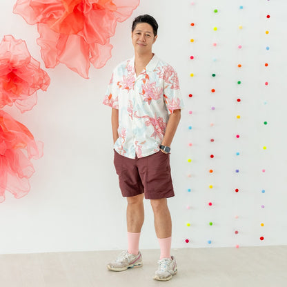 A dad stands comfortably in the men’s shirt from the Le Petit Society x Sheila Sim CNY 2026 Lotus Collection. The shirt features an all-over lotus print in soft coral, pink and blue tones, paired with a relaxed short-sleeve cut and an open collar. The loo