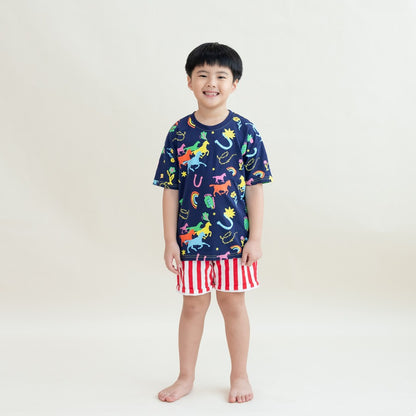 A young boy stands smiling in the Rainbow Horse tee paired with bold red-and-white striped shorts. The vibrant illustrations of horses, stars and rainbows pop against the navy base, giving the outfit a festive, playful look perfect for Lunar New Year.