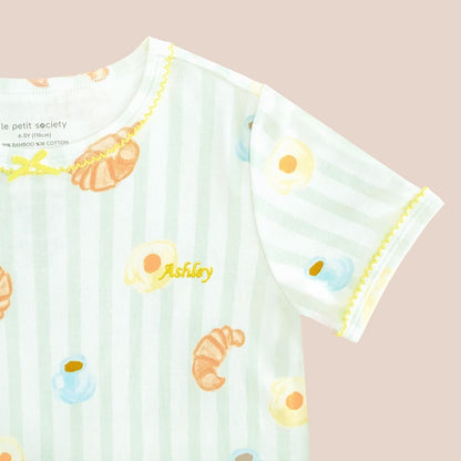 A close-up of a name embroidery personalisation on kids' dress in breakfast print by Le Petit Society.
