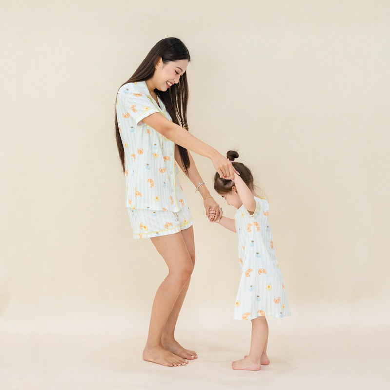 A mother and daughter wearing matching sleepwear  from Le Petit Society, featuring pastel green stripes and a print of breakfast food.