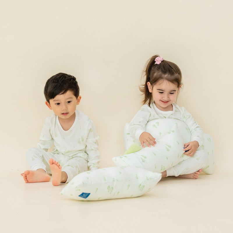 A little boy and girl holding pillows featuring a playful green pear print, from Le Petit Society.