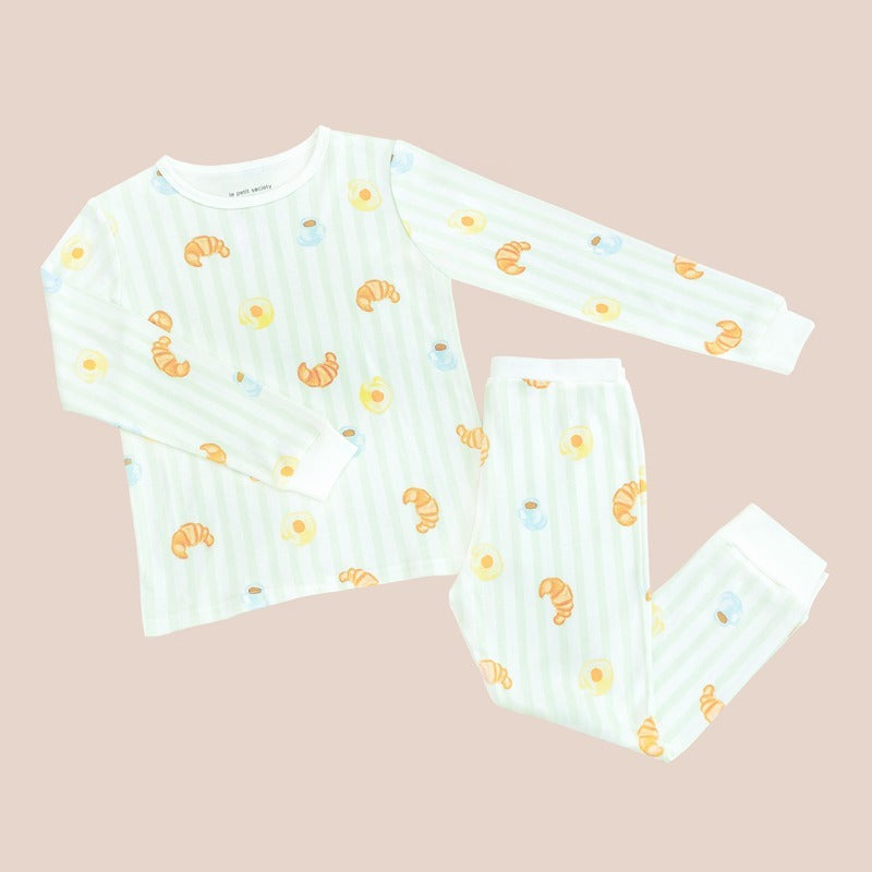 A kids' bamboo pyjamas set by Le Petit Society, featuring a print of breakfast food and pastel green stripes.
