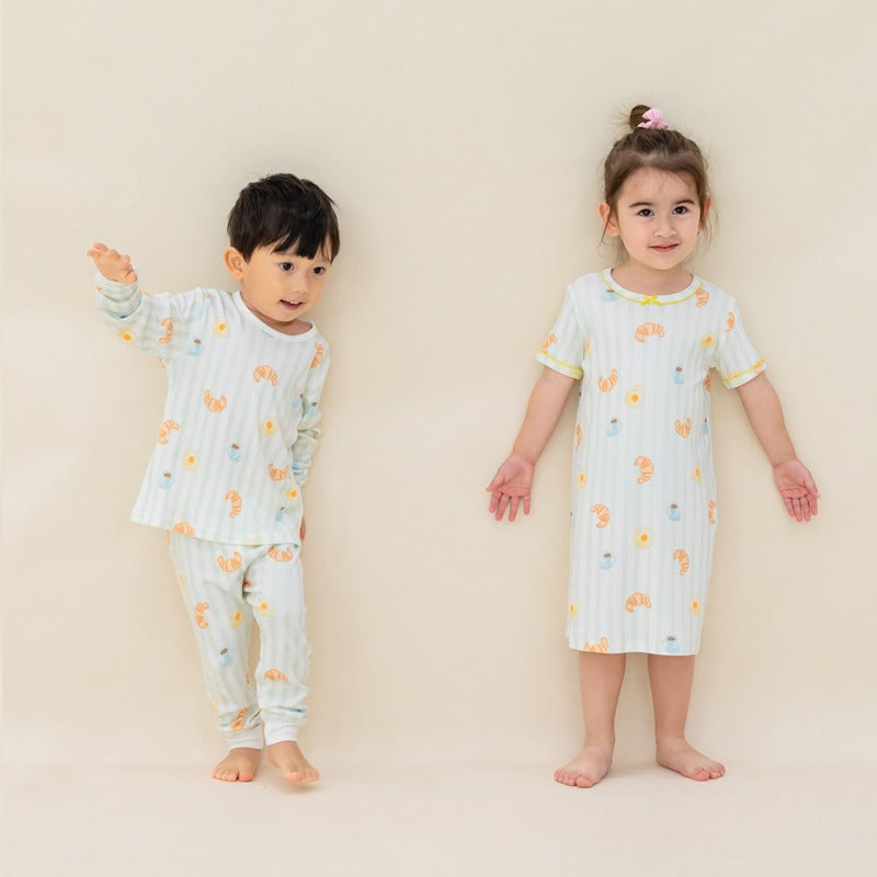 Two kids, a boy and a girl, are wearing sleepwear from Le Petit Society, featuring matching prints of breakfast food and pastel green stripes.