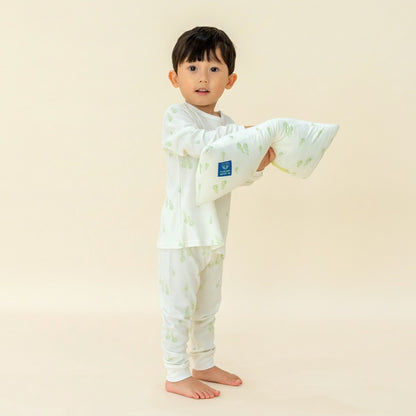 A little boy wearing a pyjamas set from Le Petit Society, with a pillow in a matching print of green pears.