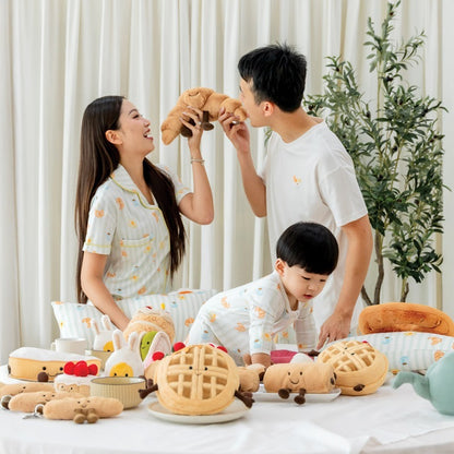 A family of three — mother, father, and baby boy — wearing matching outfits featuring a print of breakfast food from Le Petit Society.