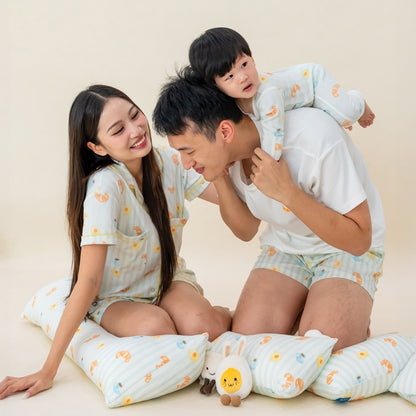 A family of three — mother, father, and baby boy — dressed in matching sleepwear from Le Petit Society, adorned with a playful breakfast food print, as they share a joyful moment together.