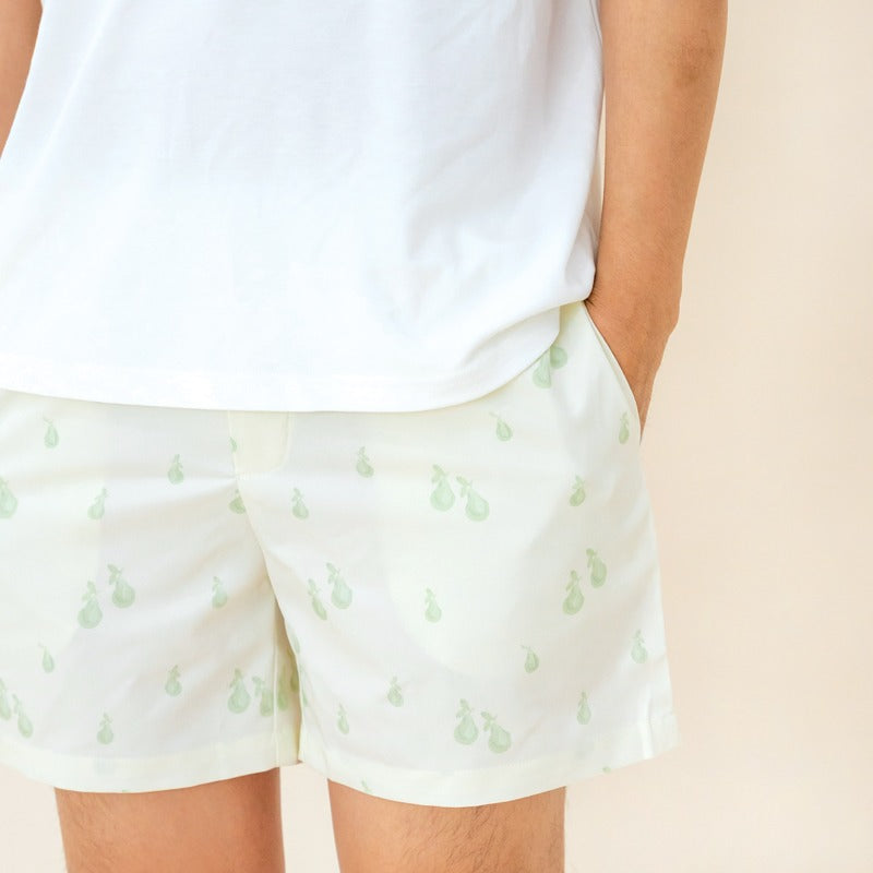 An adult male wearing a pair of lounge shorts featuring a print of pears, from Le Petit Society.