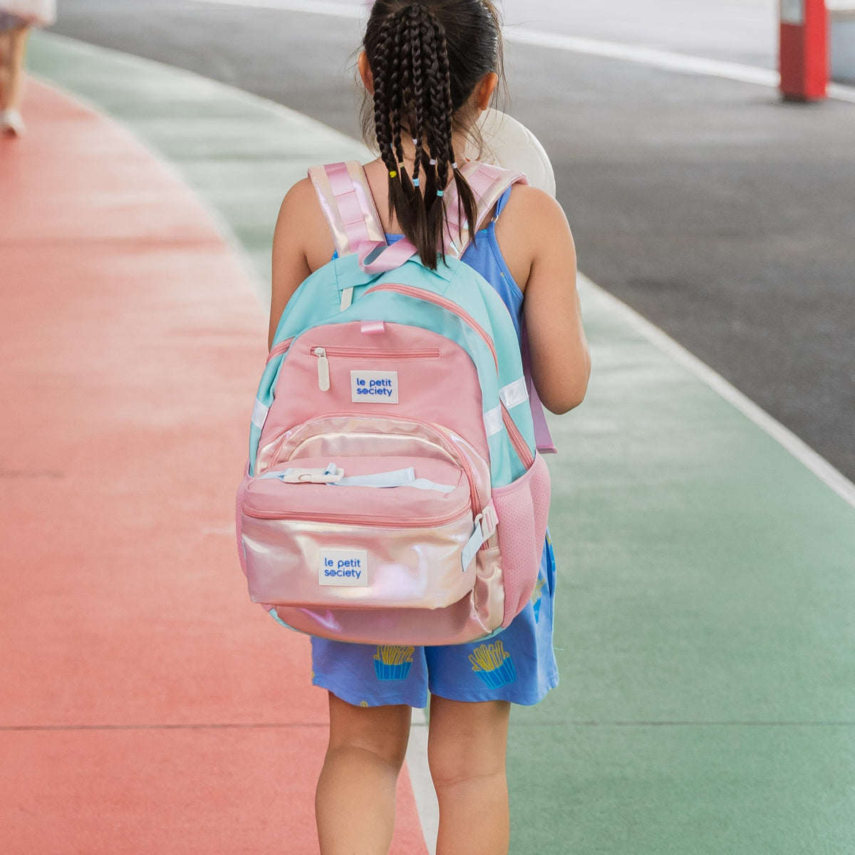 A primary school girl carrying a school bag and lunch bag set in pink by Le Petit Society.