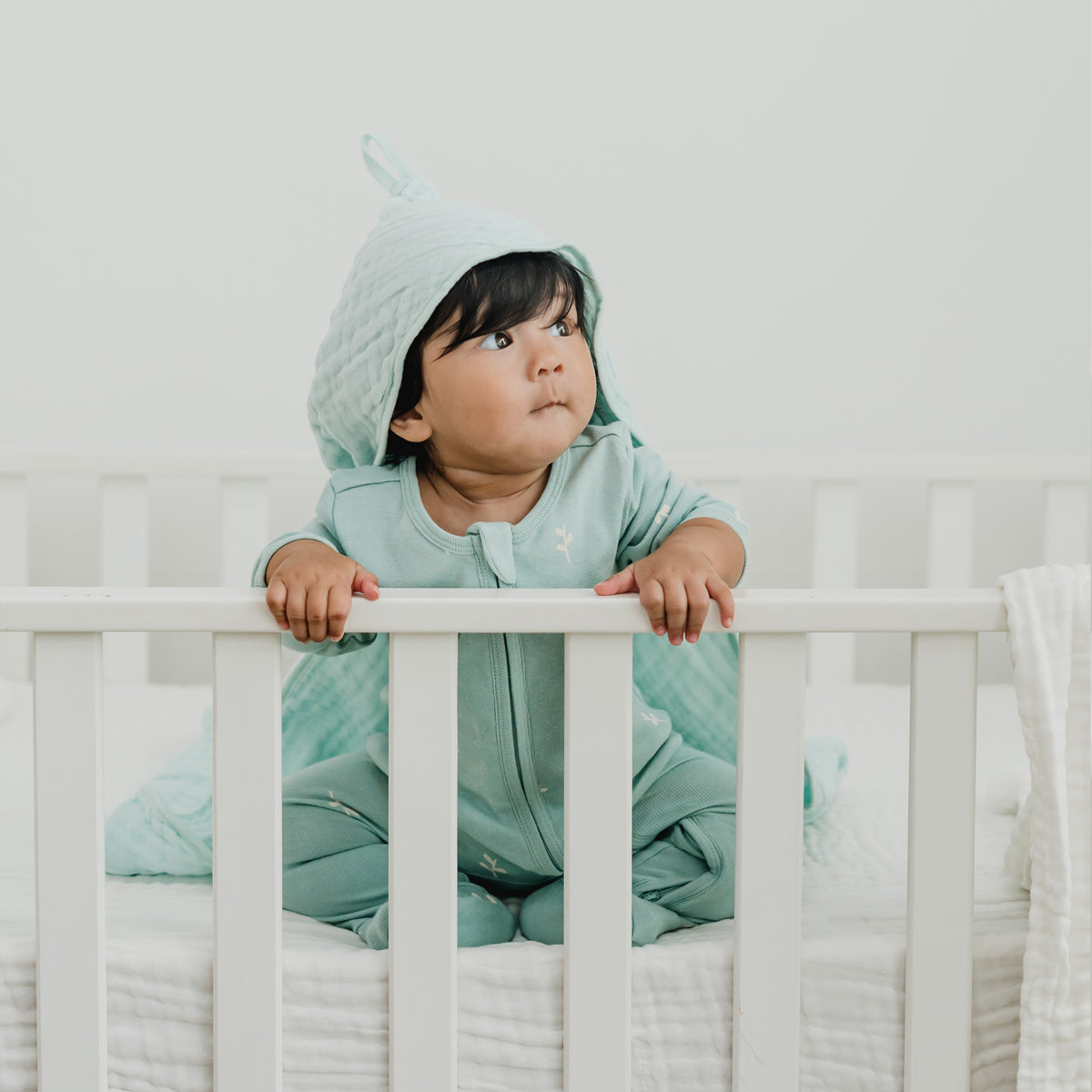 A baby wearing a mint blue organic zip sleepsuit in leaf print from Le Petit Society.