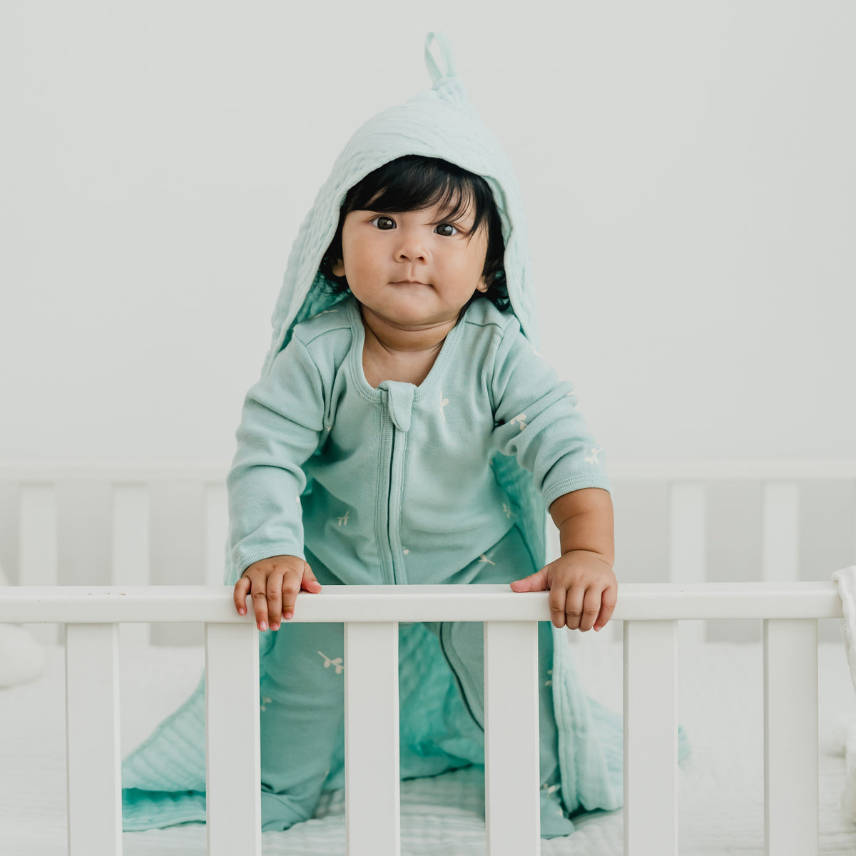 A baby wearing a mint green organic zip sleepsuit in leaf print from Le Petit Society.
